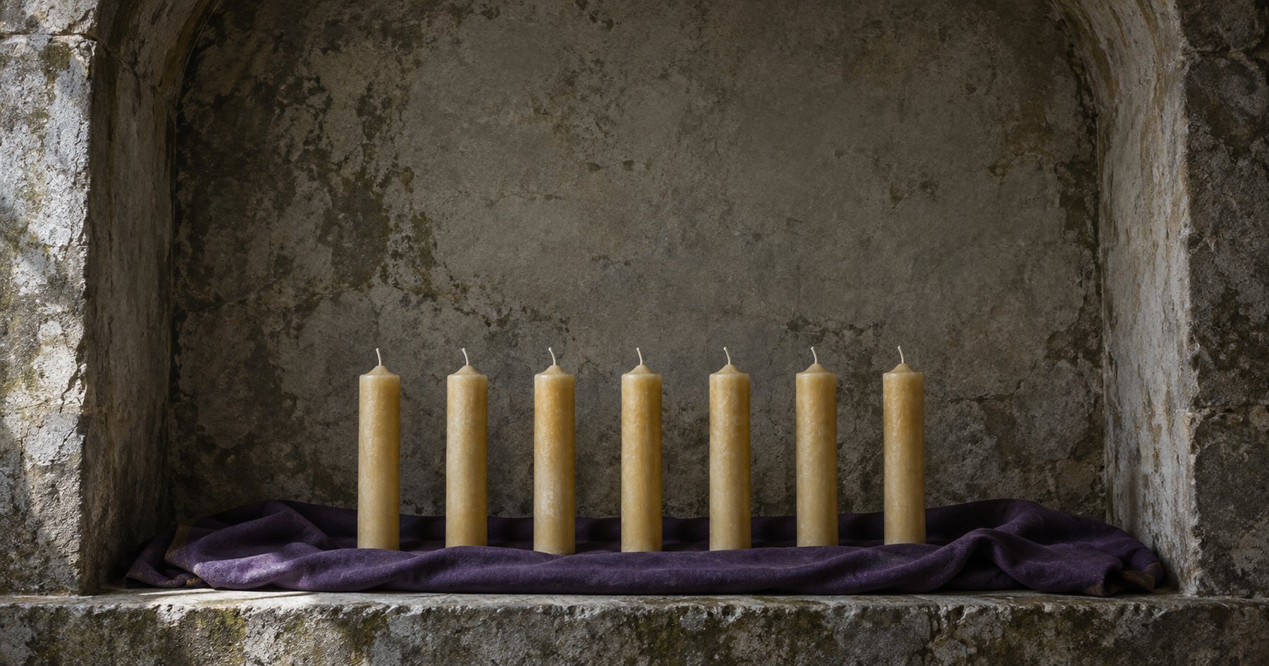 Seven plain unlit candles standing in a row in a worn stone niche, on a folded length of deep violet cloth, in cold daylight