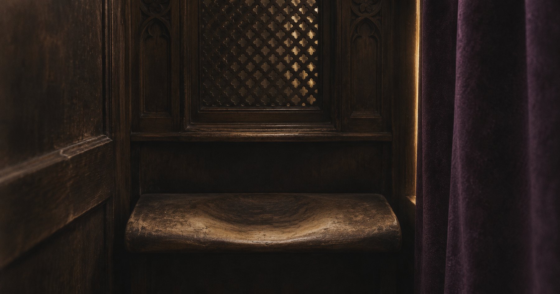The inside of a dark wooden confessional, with a carved lattice grille lit from behind and a kneeler worn pale and hollow from decades of use